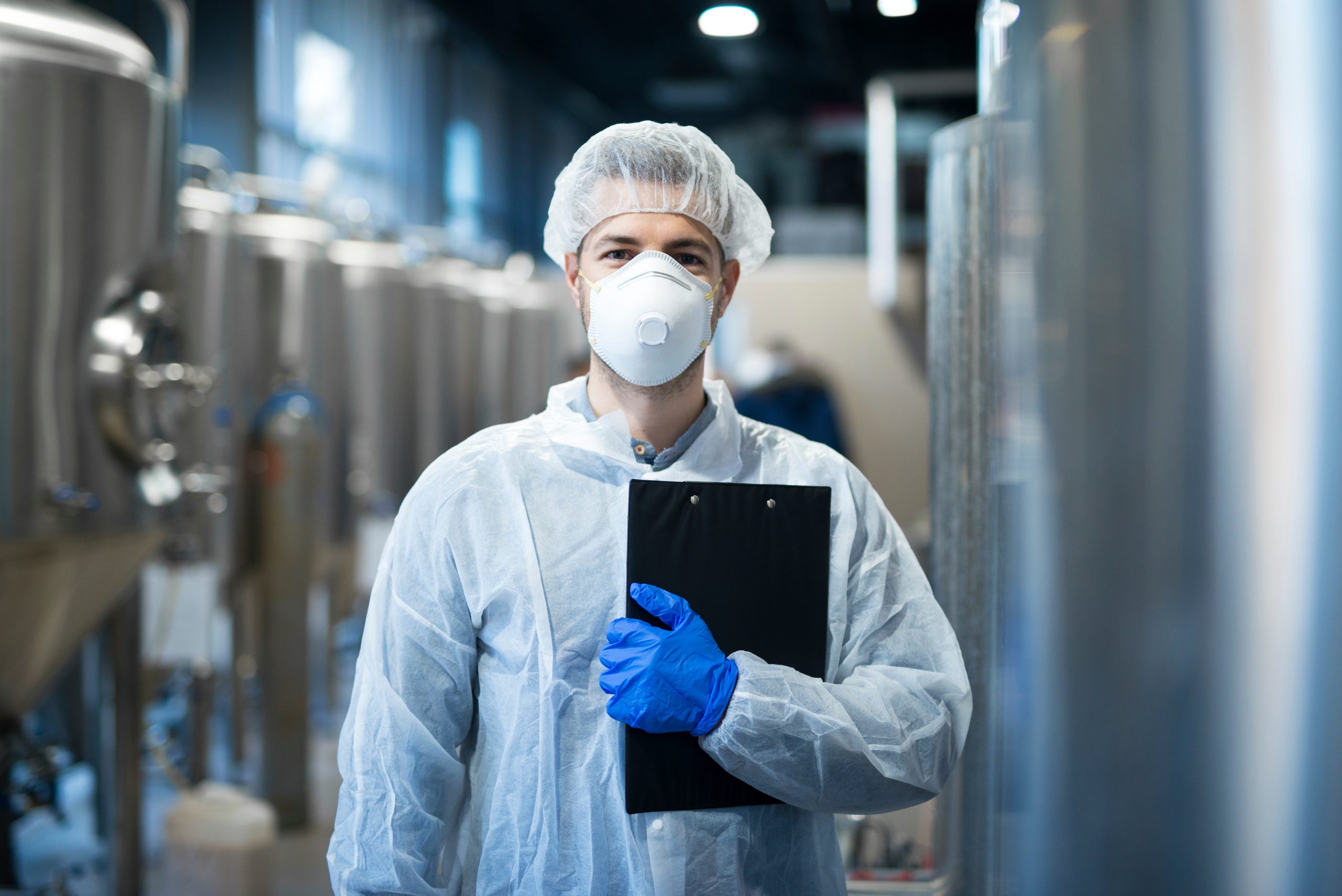 Technologist with protective mask and hairnet standing at factory production line. Food or beverage processing factory.