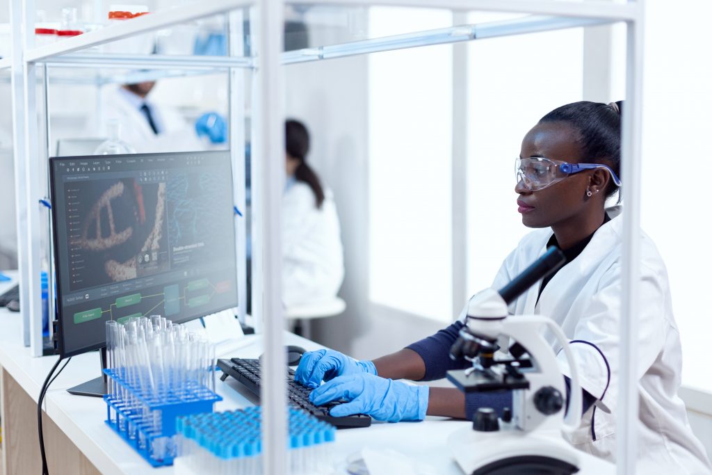 African chemist researcher typing information on computer from experimental drug trial.